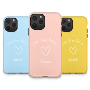 May include: Three phone cases in pastel colors: light blue, pink, and yellow. Each case has the phrase "Love Stays Strong" in white script, a white heart, and a name. The light blue case says "Heather", the pink case says "Melissa", and the yellow case says "Michelle".