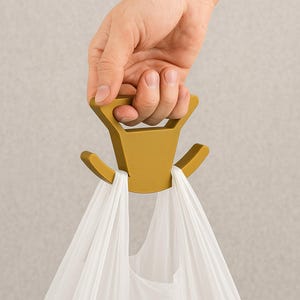May include: A mustard-colored plastic bag holder with a handle is held by a hand. Two white plastic bags are hanging from the holder. The holder has a triangular handle and two curved hooks.