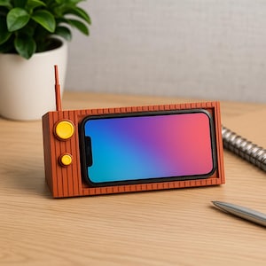 Op de afbeelding: Een telefoonstandaard in retrostijl in de vorm van een vintage radio. De standaard is gemaakt van oranje-bruin materiaal, met een sleuf voor een smartphone met een kleurrijke gradiënt. Het heeft een gele knop en een antenne.