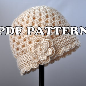 Può includere: Un cappello all'uncinetto di colore crema con un fiocco di crochet come ornamento. Il cappello è esposto su un supporto nero. Il testo "PDF PATTERN" è visualizzato nella parte superiore dell'immagine.