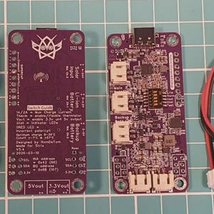 Puede incluir: Un conjunto de componentes electr&oacute;nicos, que incluyen dos condensadores, dos placas de circuito p&uacute;rpura con texto y un cable rojo y negro con conectores. Los componentes est&aacute;n dispuestos sobre un fondo de cuadr&iacute;cula.