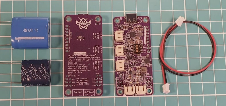 Puede incluir: Un conjunto de componentes electr&oacute;nicos, que incluyen dos condensadores, dos placas de circuito p&uacute;rpura con texto y un cable rojo y negro con conectores. Los componentes est&aacute;n dispuestos sobre un fondo de cuadr&iacute;cula.