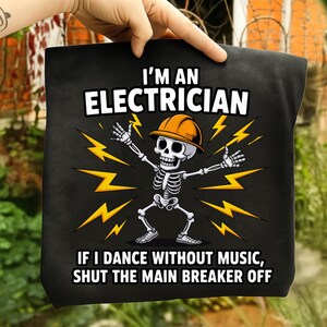 May include: Black tote bag with the text "I'M AN ELECTRICIAN" above a skeleton wearing a hard hat and surrounded by yellow lightning bolts. The text "IF I DANCE WITHOUT MUSIC, SHUT THE MAIN BREAKER OFF" is below the skeleton.
