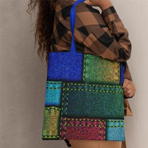 Peut inclure: Un sac fourre-tout coloré avec un motif patchwork. Le sac présente des carrés de tissu bleu, vert, jaune et rouge, cousus ensemble avec du fil jaune. Il a des poignées bleues et est porté par une personne.