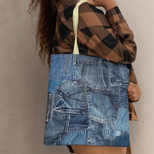 May include: A denim tote bag featuring a patchwork design of various blue jean pockets and fabric pieces. The bag has a light-colored strap and is held by a person wearing a brown and black plaid shirt.