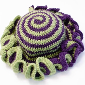 Può includere: Un cappello all'uncinetto con un motivo a spirale verde e viola e un bordo arricciato.