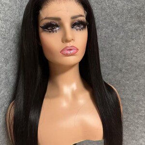 May include: A long, straight black wig with a lace front. The wig is on a mannequin head and has a natural, sleek look.