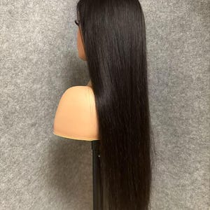 May include: A long, straight black human hair wig on a wig stand. The wig is styled in a sleek, straight style and appears to be very soft and silky.