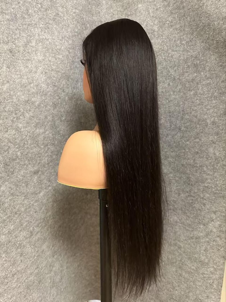 May include: A long, straight black human hair wig on a wig stand. The wig is styled in a sleek, straight style and appears to be very soft and silky.