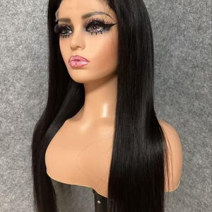 May include: A long, straight black wig with a lace front. The wig is styled in a sleek, straight style and is worn on a mannequin head.