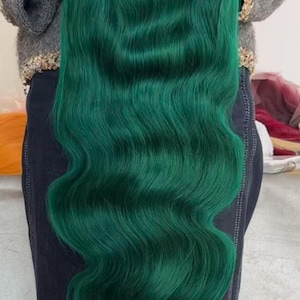 May include: A long, emerald green wig with wavy, voluminous hair. The wig is a vibrant shade of green, with a natural-looking wave pattern. The hair cascades down, creating a full and flowing appearance. The wig is likely designed for cosplay or fashion.