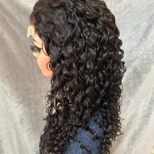 Könnte beinhalten: Dunkelbraune, lockige Perücke, die auf einem Schaufensterkopf gestylt ist. Die Perücke hat lange, voluminöse Locken und eine Lace-Front für einen natürlichen Look. Der Schaufensterkopf hat lange Wimpern und steht vor einem neutralen Hintergrund.