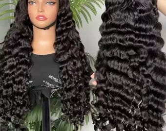 May include: A black, long, wavy wig displayed on a mannequin head and held up. The wig features a lace front and a deep wave pattern. The hair is a rich, dark black colour, and the waves are voluminous and well-defined. The wig is styled to fall past the shoulders.