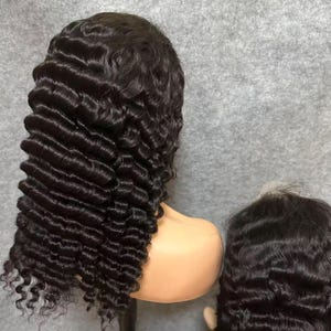 May include: A dark brown, curly wig styled on a mannequin head. The wig features tight, defined curls and a natural-looking hairline. The hair is a rich, dark color, and the curls cascade down the sides and back of the head.