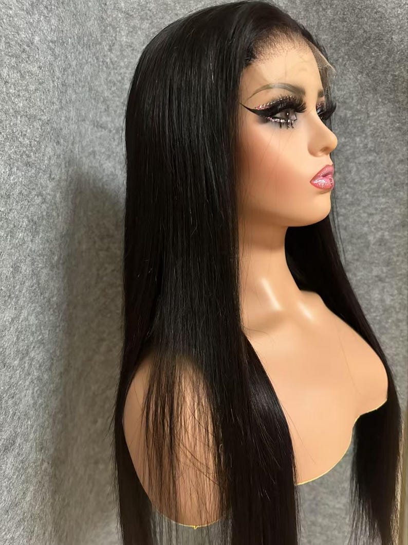 May include: A long, straight black wig with a lace front. The wig is styled with a centre parting and falls to the shoulders.