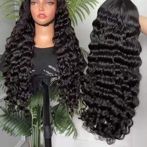 May include: A black, long, wavy wig on a mannequin head and a separate wig held by a hand. The wig features a lace front and a deep wave pattern. The hair is a rich, dark black color, and the waves are tightly curled.