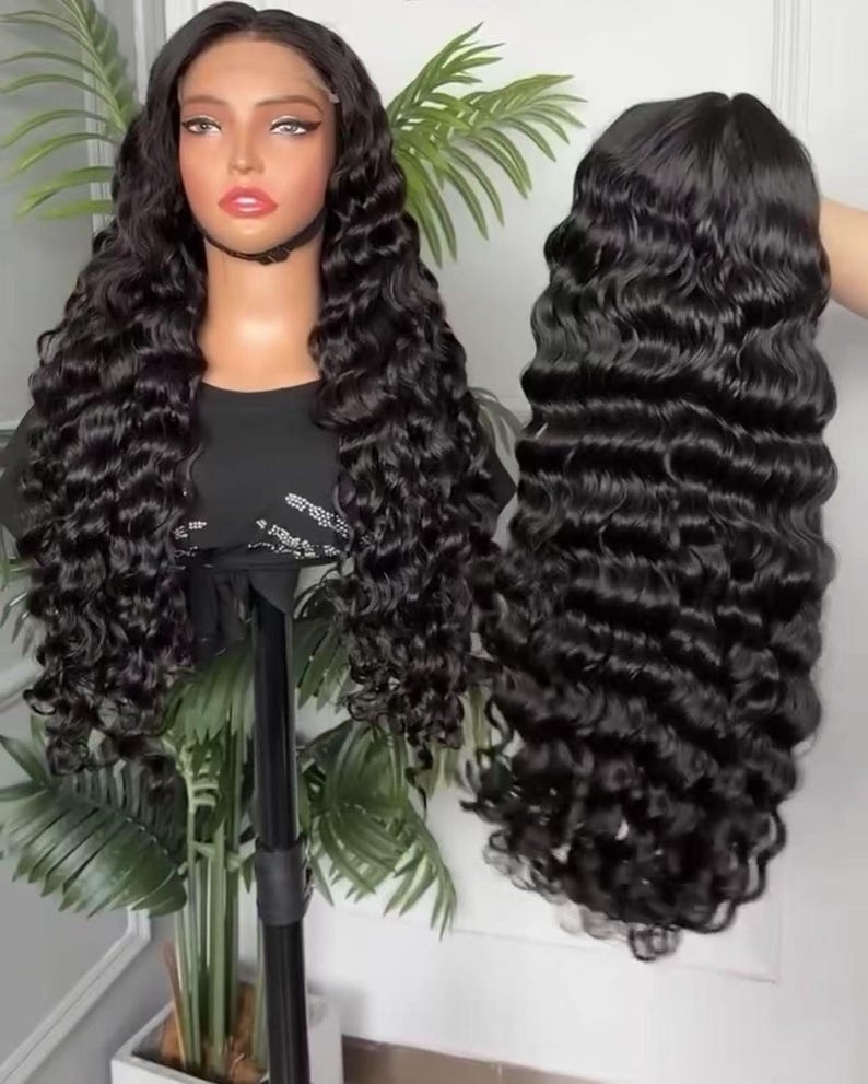 May include: A black, long, wavy wig on a mannequin head and a separate wig held by a hand. The wig features a lace front and a deep wave pattern. The hair is a rich, dark black color, and the waves are tightly curled.