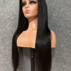 May include: A long, straight black human hair wig on a mannequin head. The wig is styled with a middle parting and has a natural, sleek look.
