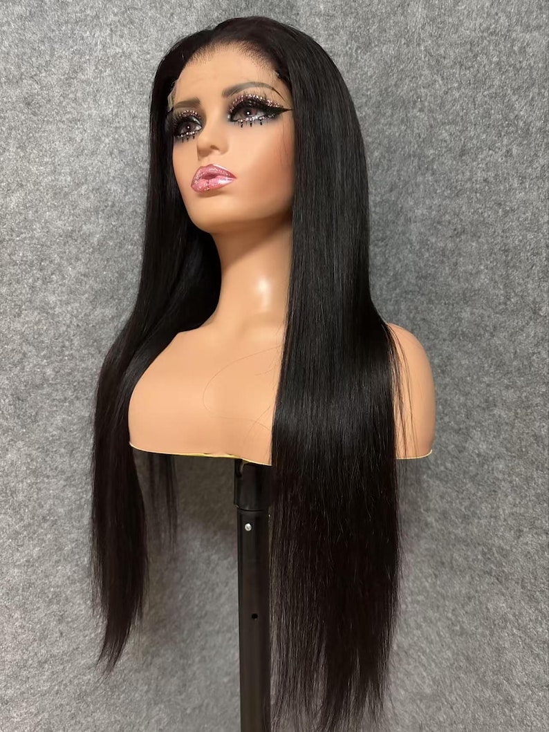 May include: A long, straight black human hair wig on a mannequin head. The wig is styled with a middle parting and has a natural, sleek look.