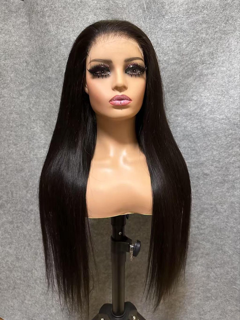 May include: A long, straight black human hair wig on a mannequin head. The wig is styled with a middle parting and has a natural, sleek look.