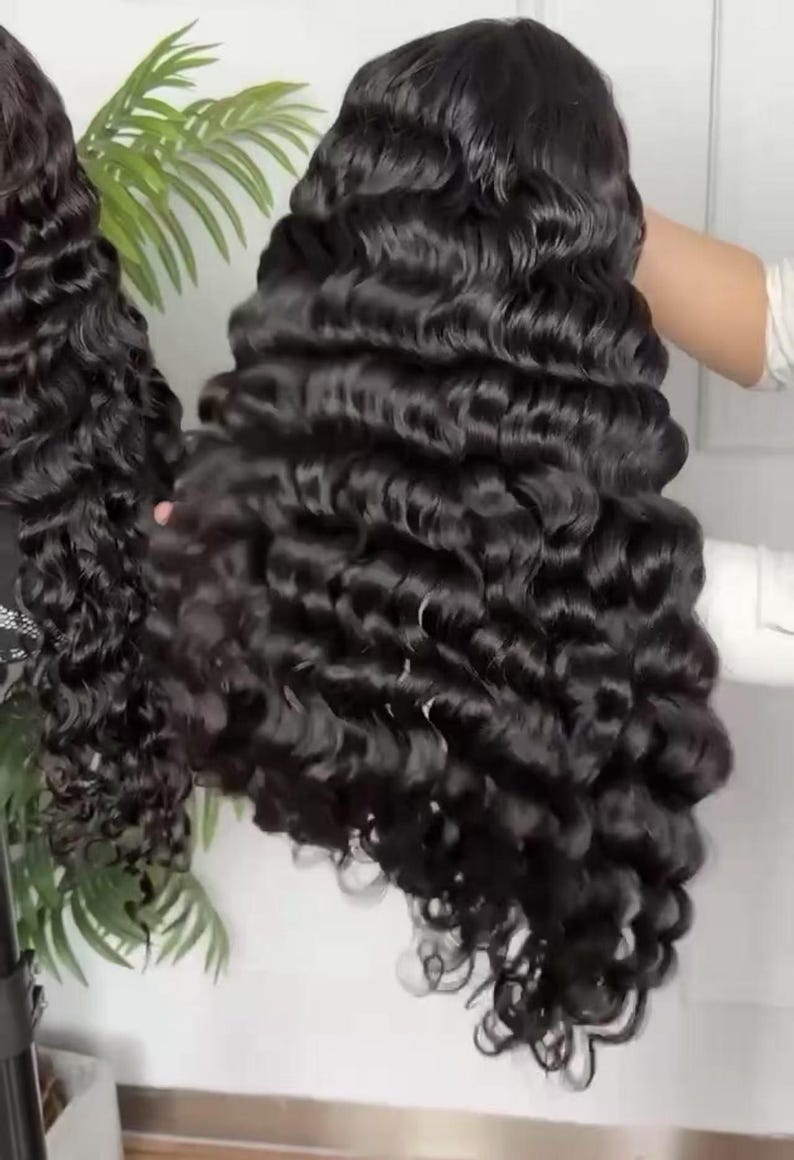 May include: A long, wavy black wig with voluminous curls. The wig is held up, showcasing the texture and style of the hair. The curls are tightly wound and cascade down, creating a full and glamorous look.