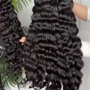 May include: A long, black, wavy wig with a deep wave pattern. The wig is styled with voluminous curls and appears to be made of synthetic or human hair. The hair is a rich, dark color and has a natural-looking sheen. The wig is likely designed for fashion or cosplay.