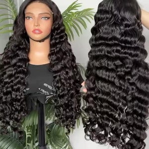 May include: A black, long, wavy wig displayed on a mannequin head and held up. The wig features a lace front and a deep wave pattern. The hair is a rich, dark black color, and the waves are voluminous and well-defined. The wig is styled to fall past the shoulders.