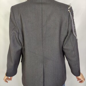 Puede incluir: Un blazer gris oscuro con finas rayas verticales. El blazer presenta una cadena decorativa y detalles de perlas en el hombro. Las mangas tienen pu&ntilde;os abotonados. Un blazer de estilo cl&aacute;sico con un toque moderno.