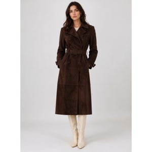 May include: A dark brown suede trench coat featuring a double-breasted front, a wide notched collar, long sleeves with buckled cuffs, and a matching fabric belt with a rectangular buckle at the waist, paired with cream-colored knee-high boots.