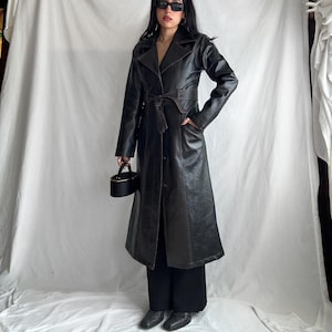 May include: A long black leather trench coat with brown stitching and a belt. The coat has a classic design with a collar, lapels, and pockets.