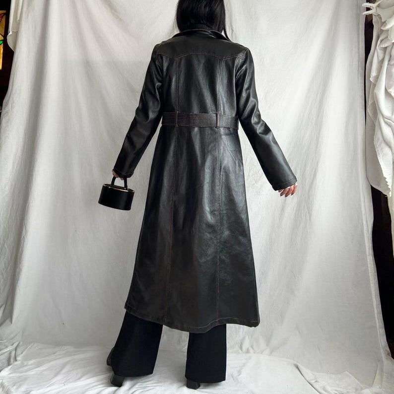 May include: A long black leather trench coat with a belt and a small black purse.