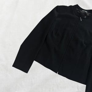 Peut inclure: Une veste noire zipp&eacute;e avec un col montant. La veste est cintr&eacute;e et de longueur courte.