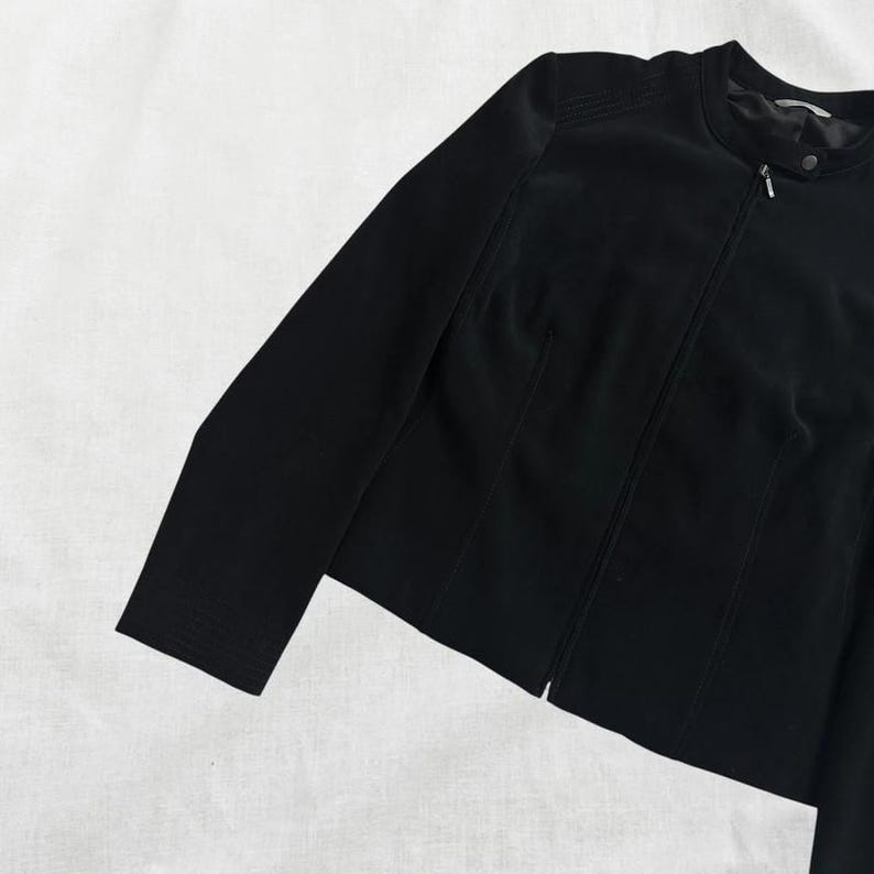 Peut inclure: Une veste noire zipp&eacute;e avec un col montant. La veste est cintr&eacute;e et de longueur courte.