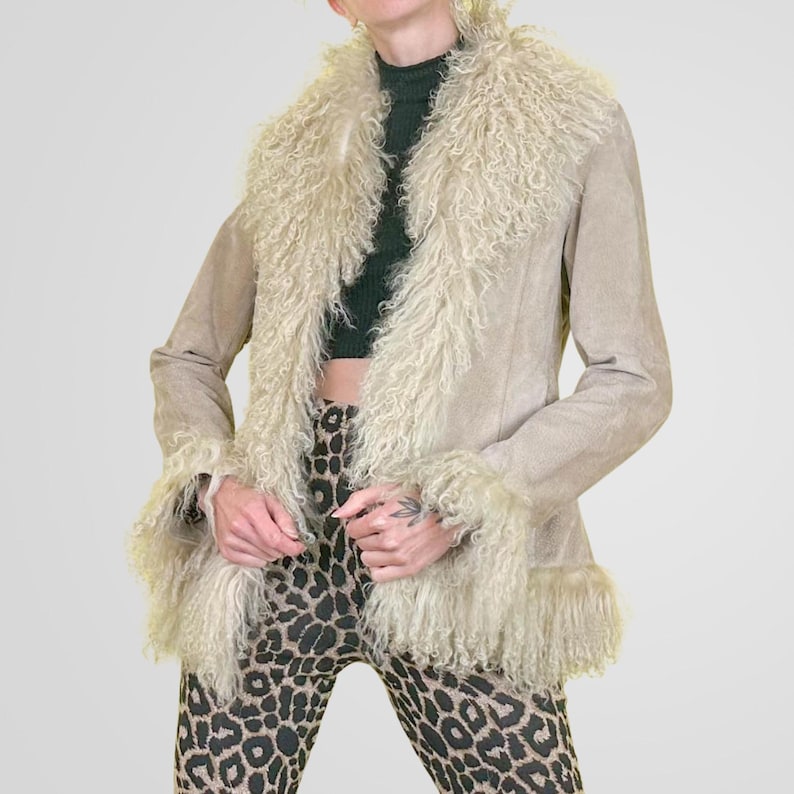 May include: A tan suede jacket with a cream-colored, shaggy fur collar and cuffs. The jacket has a classic design and is worn over a dark green top and leopard print pants. The jacket is a vintage piece.