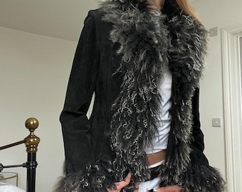 Puede incluir: Chaqueta de ante negra con cuello y puños de piel sintética. La chaqueta presenta un corte entallado y un ribete de piel gris y negra en contraste. Una prenda de abrigo elegante.
