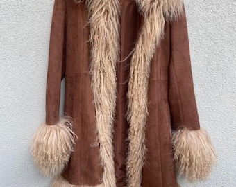 May include: A brown suede coat with a faux fur trim and cuffs. The coat has a longline silhouette with a hood and a light brown fur trim that extends down the front. The cuffs and hemline also feature the same light brown fur.