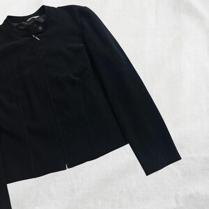 Peut inclure: Une veste noire zipp&eacute;e avec un col montant et des manches longues.