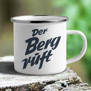 May include: White enamel mug with a silver rim. The mug has black text that reads "Der Berg ruft" which translates to "The mountain calls".
