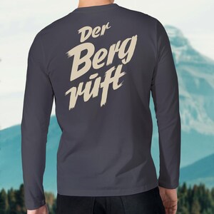 May include: A dark blue long-sleeved shirt with the text "Der Berg ruft" in a cream color on the back.