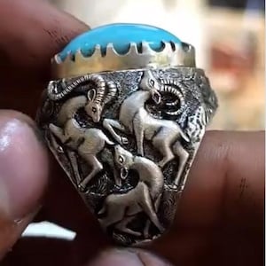 May include: Silver ring with a turquoise stone and detailed relief of three mountain goats. The ring has a detailed, antique design. The turquoise stone is oval-shaped and set in a silver bezel.