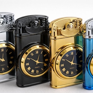 Op de afbeelding: Vier metalen aanstekers in zilver, zwart, goud en blauw. Elke aansteker heeft een klok met Romeinse cijfers en gouden wijzers. De klok is geplaatst in een goudkleurige rand.