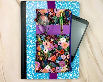 Könnte beinhalten: Ein blaues Notizbuch mit einem violetten Gummiband, das eine florale Stofftasche hält. Die Tasche hat einen dunkelvioletten Hintergrund mit bunten Blumen, einer Brille, einem grünen Stift und einem eingesteckten schwarzen Tablet.