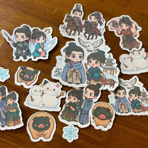 May include: A collection of colorful stickers featuring anime-style characters in various poses. The stickers depict couples, animals, and winter-themed elements like snowmen and snowflakes. The characters are dressed in traditional clothing.