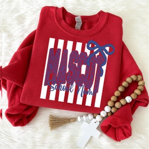 Op de afbeelding: Een rood sweatshirt met ronde hals en een grafische print van verticale witte strepen achter het woord MASCOT in een blauw luipaardpatroon, met een blauwe strik en de tekst School Name in blauw cursief schrift onder het woord.