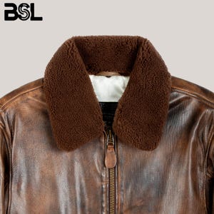 May include: Close-up of a brown leather jacket with a shearling collar. The jacket has a zipper closure and a distressed finish. The letters "BSL" are in the upper left corner.