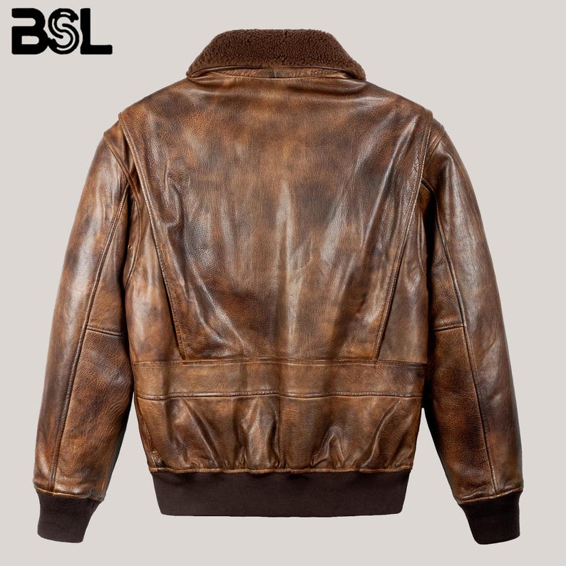 May include: A brown leather bomber jacket with a shearling collar. The jacket has a distressed finish, ribbed cuffs, and a ribbed hem. The BSL logo is in the upper left corner. The jacket is a classic style.