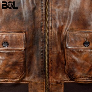 May include: Close-up of a brown leather jacket with a distressed finish. The jacket features two front pockets with button closures, a zipper closure, and a ribbed hem. The letters "BSL" are visible in the upper left corner.
