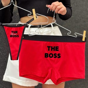 May include: A red underwear set with black trim, featuring the text "THE BOSS" on the boxer shorts and "The Real Boss" on the thong. The set is displayed on hangers.