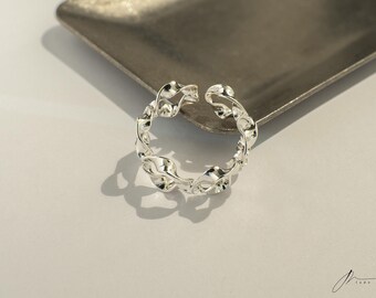 May include: A silver ring with a twisted, chain-like design. The ring is open and adjustable.