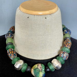 Peut inclure: Un collier coloré composé de diverses perles. Le collier comprend des perles vertes, argentées et à motifs. Les perles sont enfilées pour créer un accessoire unique et accrocheur. Le collier est présenté sur un mannequin.